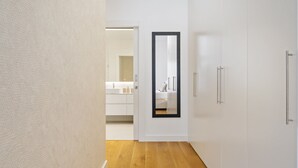 A hallway with a wooden floor, white walls, and a mirror on the wall. There is a door leading to a bathroom with a white sink and mirror. - Acqua s Bliss by Homie (Funchal)