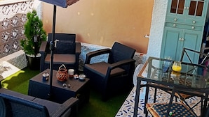 An outdoor patio with wicker furniture, a glass table, and a large umbrella. - Bungalow in La Marina Free Cancellation (San Fulgencio)