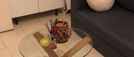 A glass-top coffee table with wooden legs, a woven basket, and a small vase with flowers.