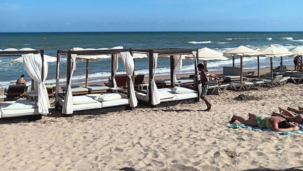 A beach with several wooden beds with white canopies, arranged in rows along the shore. - Bungalow in La Marina Free Cancellation (San Fulgencio)