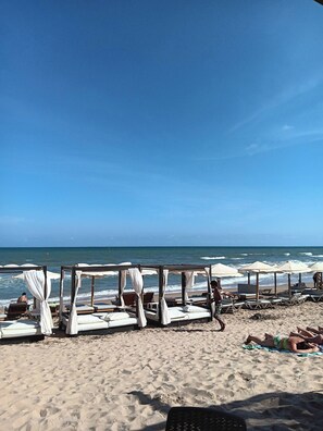 A beach with several wooden beds with white canopies, arranged in rows along the shore.