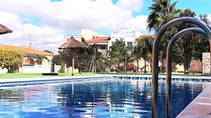 A swimming pool with a metal ladder, surrounded by buildings and palm trees. - Bungalow in La Marina Free Cancellation (San Fulgencio)