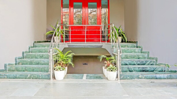 Una escalera con una puerta roja en la parte superior, plantas en macetas abajo y una barandilla de metal.