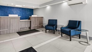 A reception area with a blue accent wall, wooden cabinets, two blue armchairs, a small round table, and a modern air conditioning unit.