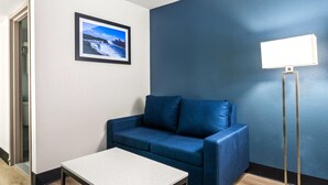 A room with a blue sofa, a small table, a framed picture on the wall, and a floor lamp.