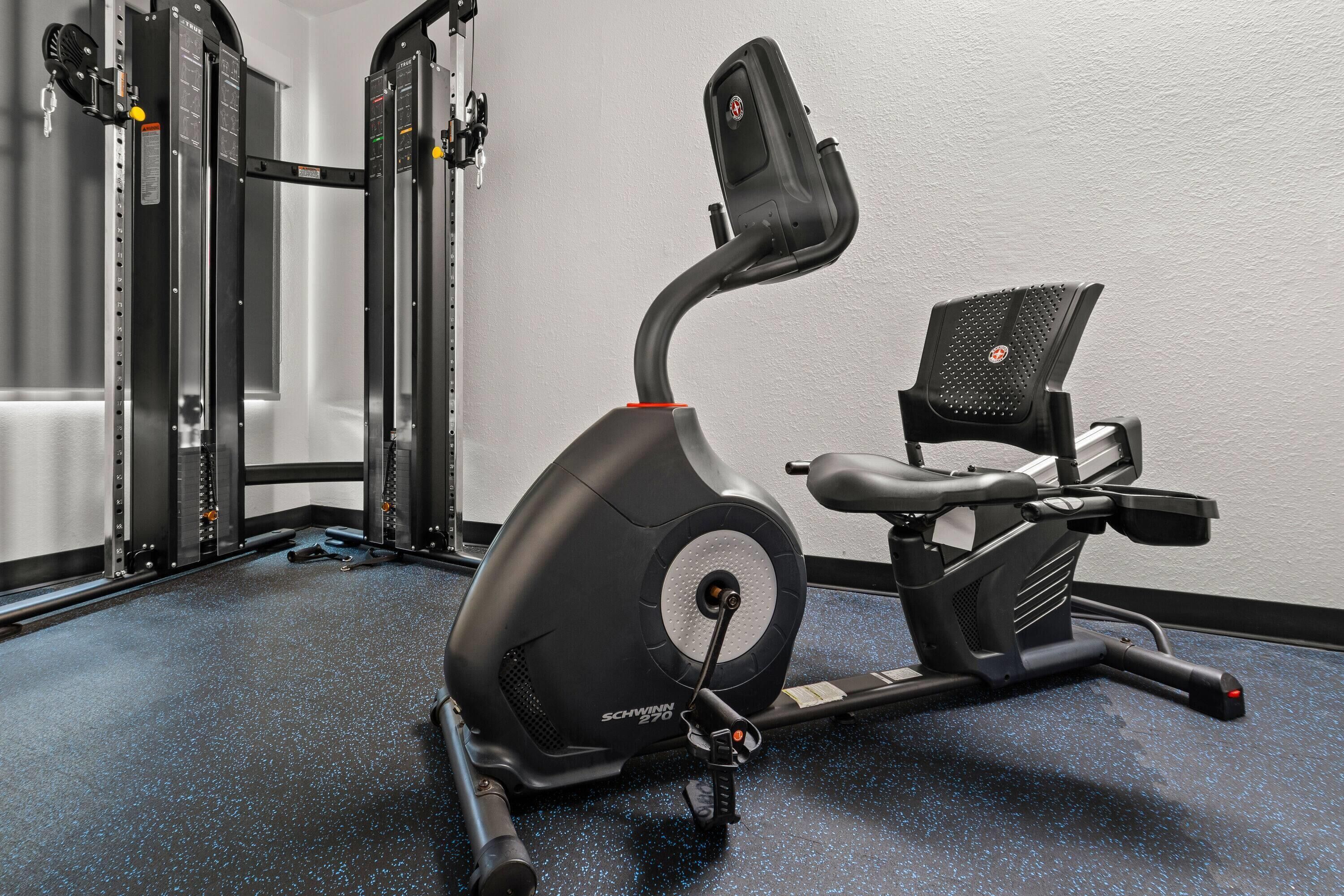 Una bicicleta estática con pantalla digital, una máquina de pesas fijada a la pared y un banco.