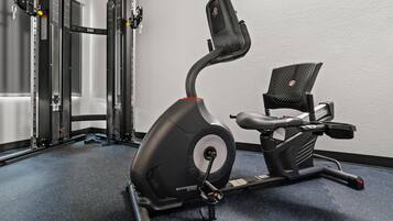Una bicicleta estática con pantalla digital, una máquina de pesas fijada a la pared y un banco.