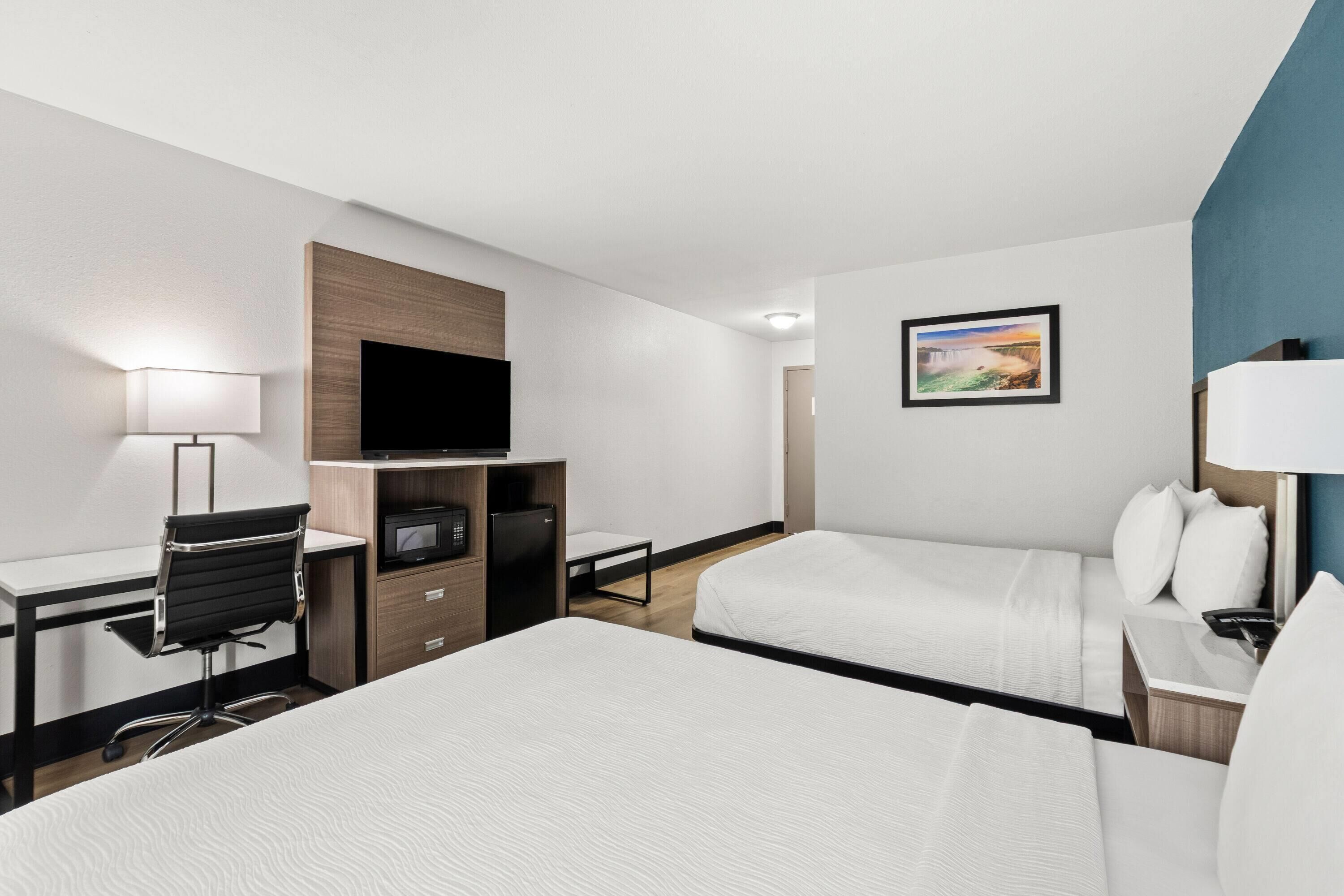 Une chambre d’hôtel avec deux lits, un bureau avec une chaise, une télévision et une petite table.