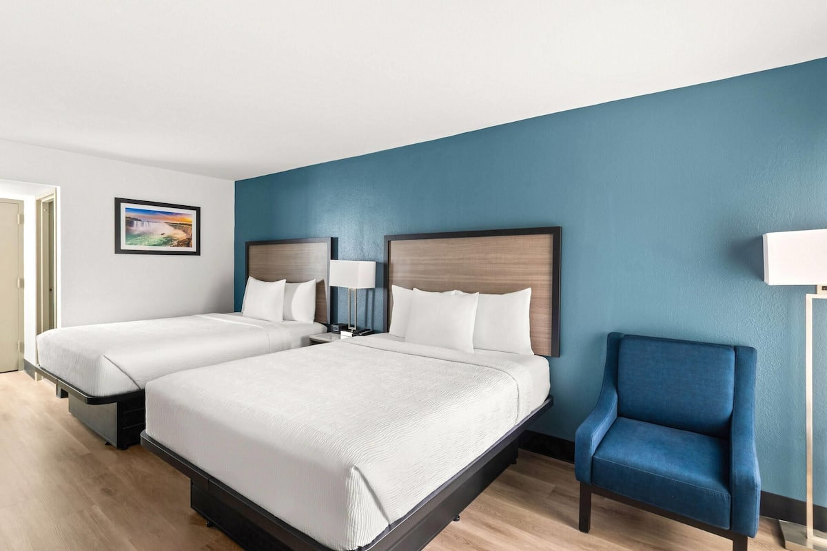 Habitación de hotel con dos camas, una pared azul, suelo de madera y un sillón azul.