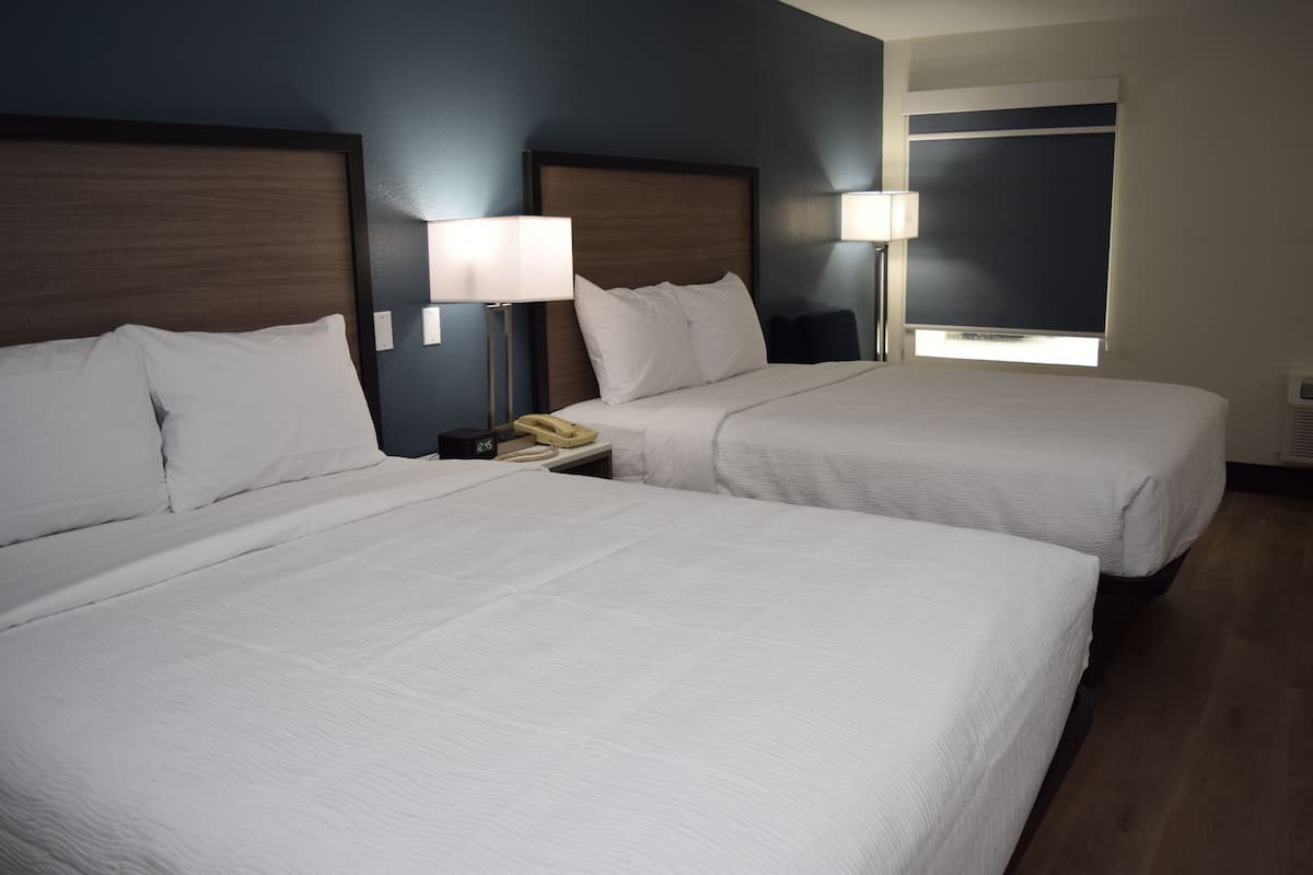 Una habitación de hotel con dos camas, una mesita de noche con teléfono y una ventana con persianas.
