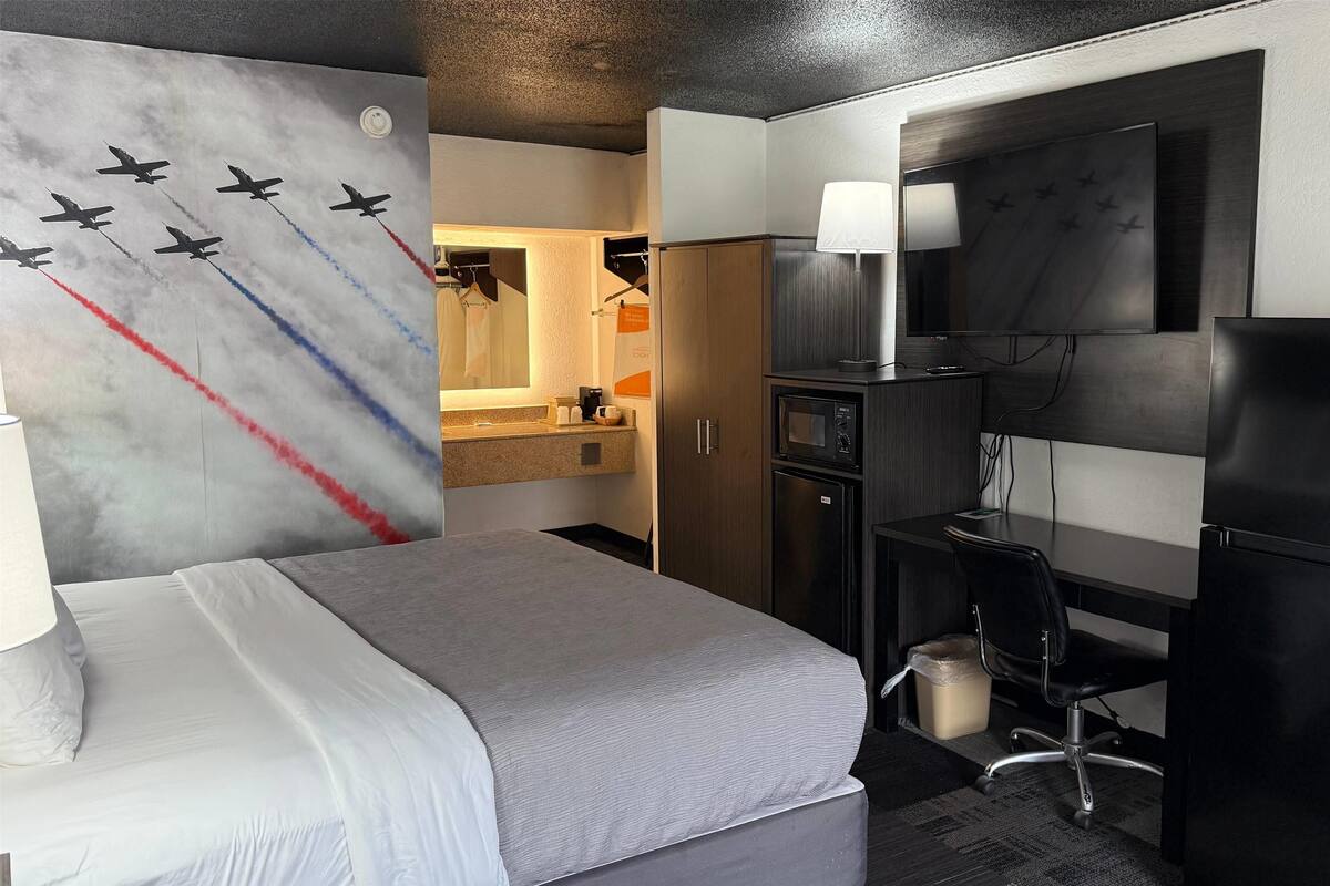 Una camera d'albergo con un letto, una scrivania, una TV, un forno a microonde e angolo cottura.