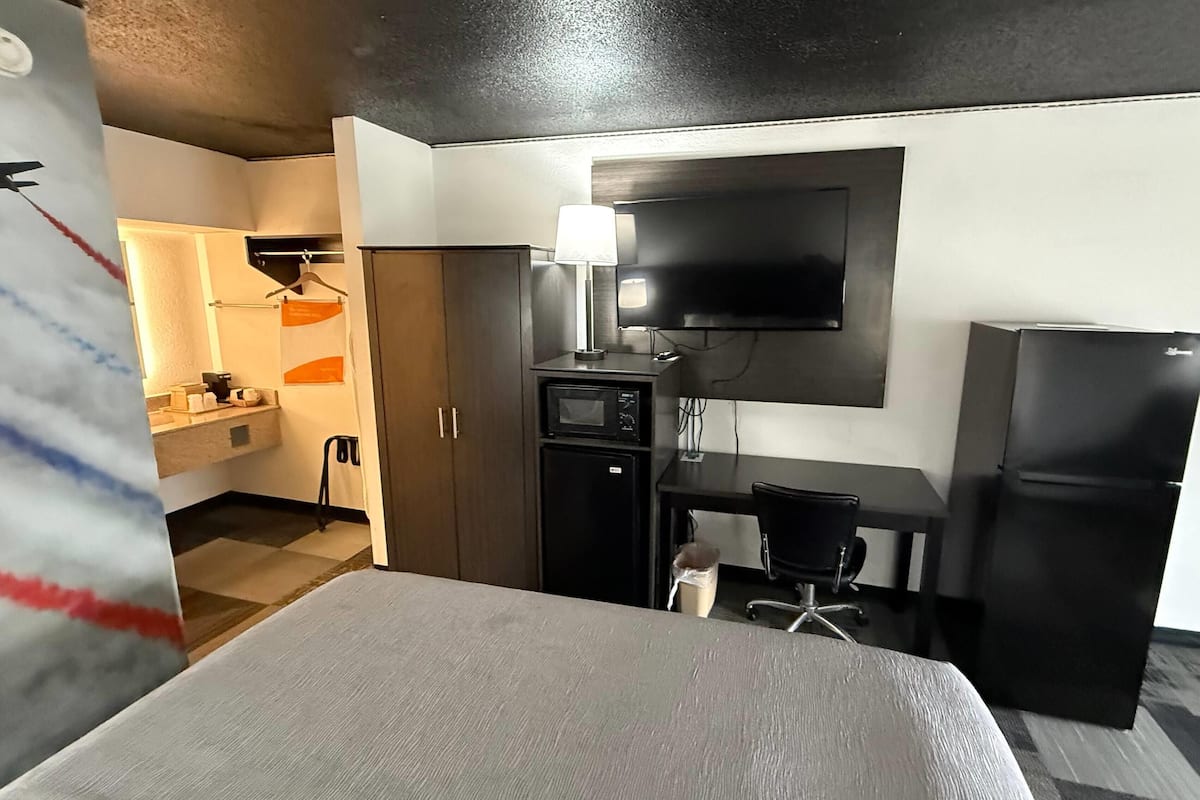 Una camera d'albergo con un letto, una scrivania, una TV, un forno a microonde, un frigorifero e un armadio.