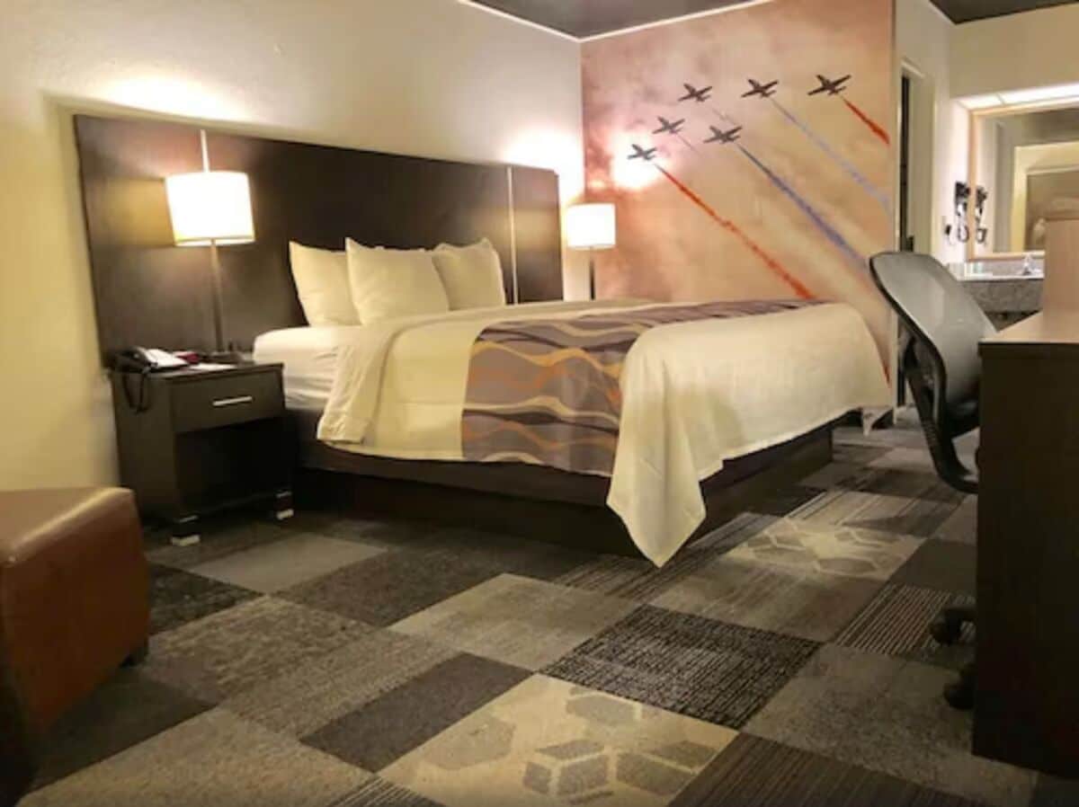 Habitación de hotel con una cama grande, dos lámparas de noche, un escritorio con silla y piso alfombrado.