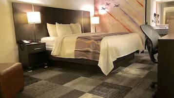 A hotel room with a large bed, two bedside lamps, a desk with a chair, and a carpeted floor.