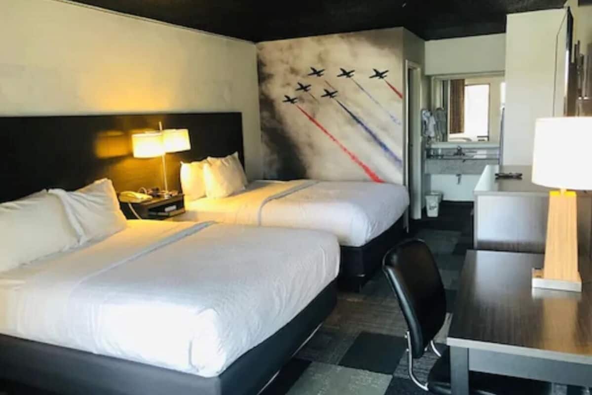 Camera d'albergo con due letti, una scrivania, una sedia e un affresco raffigurante aerei.