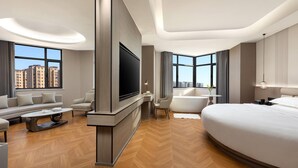 Une chambre d’hôtel moderne dotée d’un grand lit, d’un téléviseur à écran plat, d’un canapé, d’une table basse et offrant une vue sur le paysage urbain.