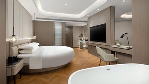 Une chambre d’hôtel moderne dotée d’un lit aux lignes courbes, d’un grand téléviseur à écran plat, d’un bureau avec une lampe et d’une salle de bain séparée.