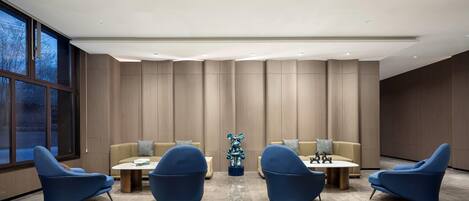 A modern lounge area with blue armchairs, a central table, and a decorative bear sculpture.