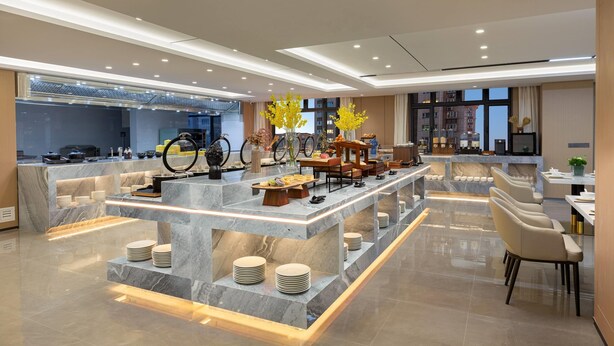 Un hall d’hôtel moderne avec un comptoir de réception en marbre, un espace salon et une vue sur le paysage urbain grâce à de grandes fenêtres.