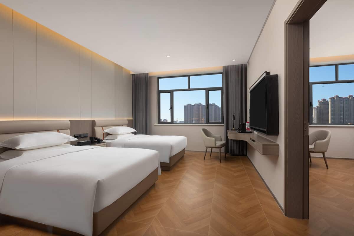 A hotel room with two beds, a TV, a desk, and a view of a cityscape.