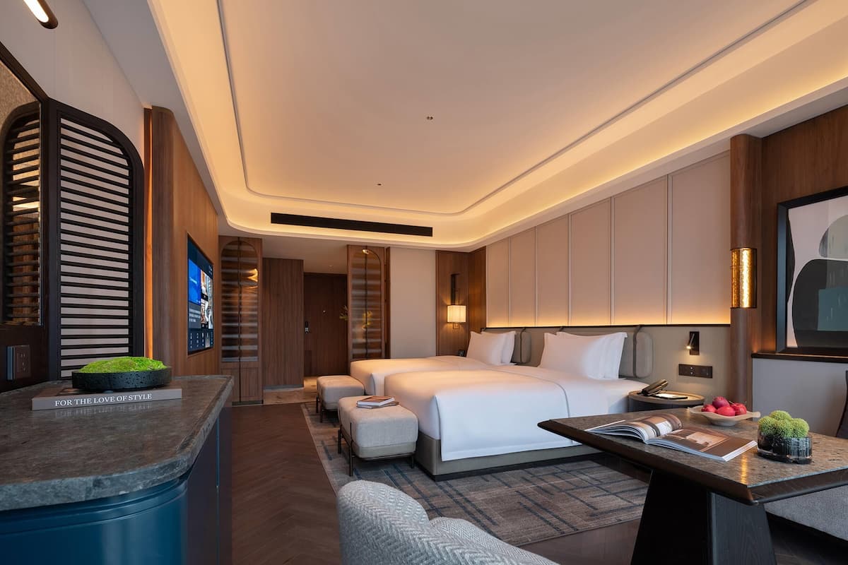 A modern hotel room with a large bed, a desk with a computer, a seating area, and a television.