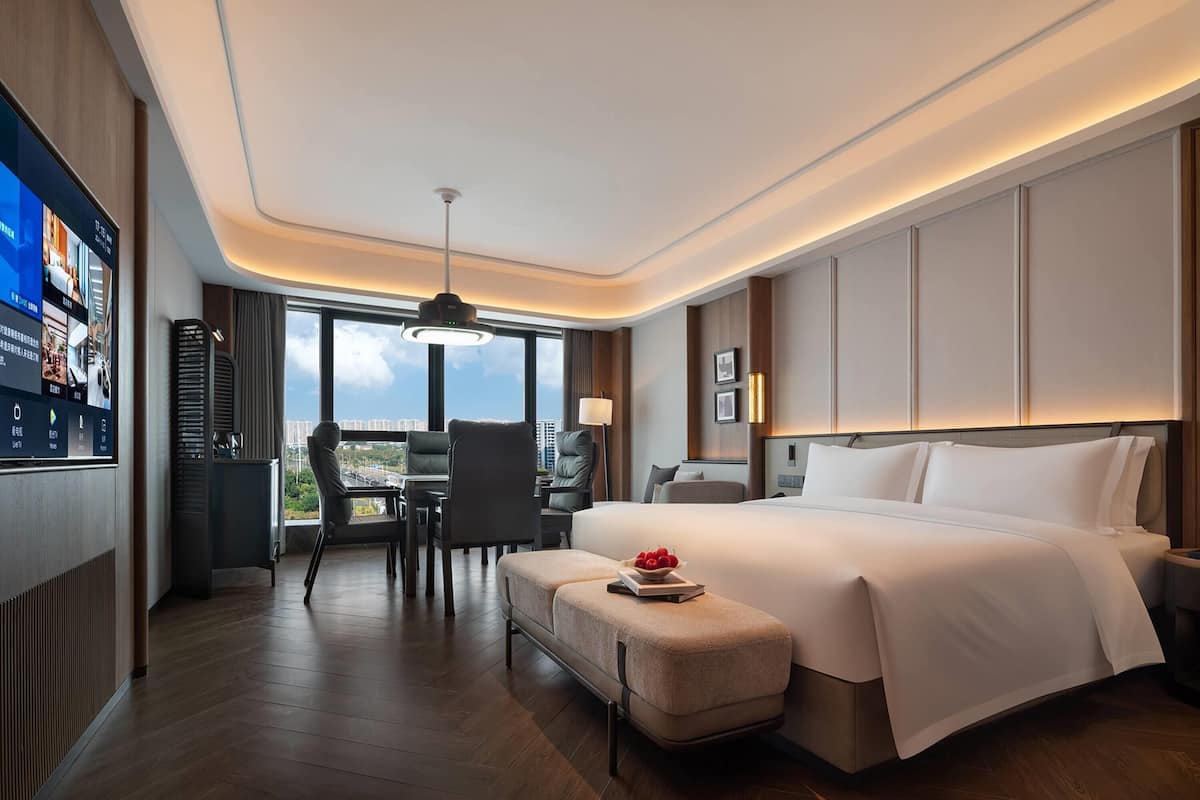 A modern hotel room with a large bed, a desk, and a view of the city.