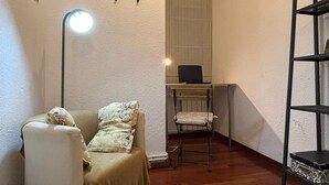A corner room with a sofa, a standing lamp, a television on a shelf, and a metal shelf unit. - "Domus Font" - Apartment in Plaça de la Font (Tarragona)