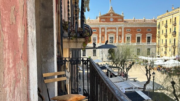 A balcony with two cushions, a railing, and a view of a plaza with buildings and umbrellas. - "Domus Font" - Apartment in Plaça de la Font (Tarragona)