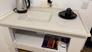 Une cuisine avec un plan de travail blanc, une bouilloire, une machine à café et un évier.