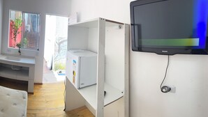 Un couloir étroit avec un banc blanc, une fenêtre ornée d’un rideau rouge, un lavabo blanc et un téléviseur fixé au mur.