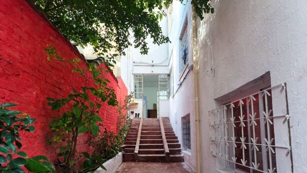 Une ruelle étroite, avec un mur rouge d’un côté et un mur blanc de l’autre. Des marches mènent à une porte située au fond de la ruelle.