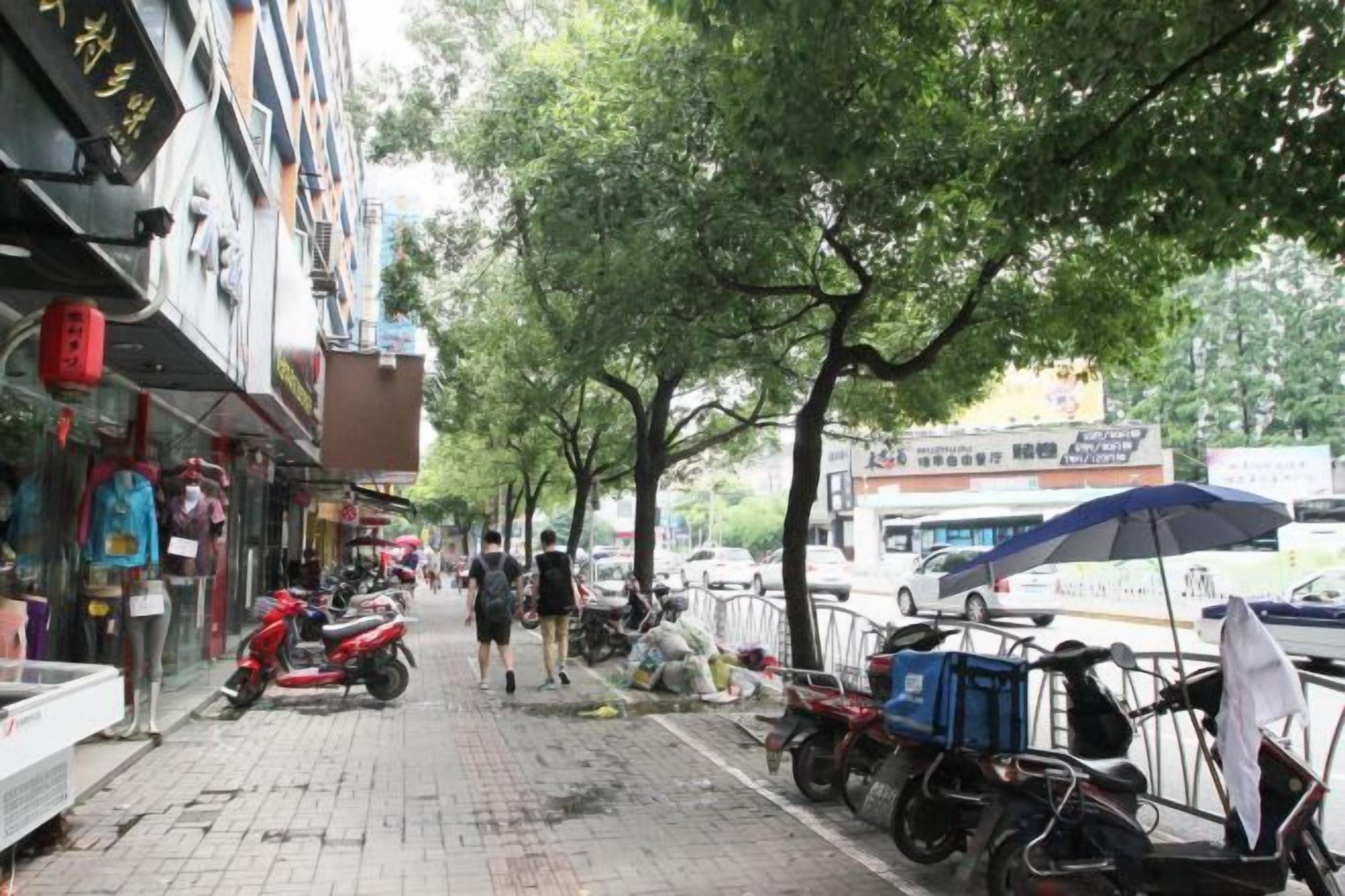 Un trottoir bordé de boutiques et de véhicules en stationnement, notamment des motos et des vélos.