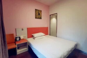 Ein Einzelbett mit weißer Matratze und einem roten Kopfteil in einem Zimmer mit rosafarbenen Wänden.