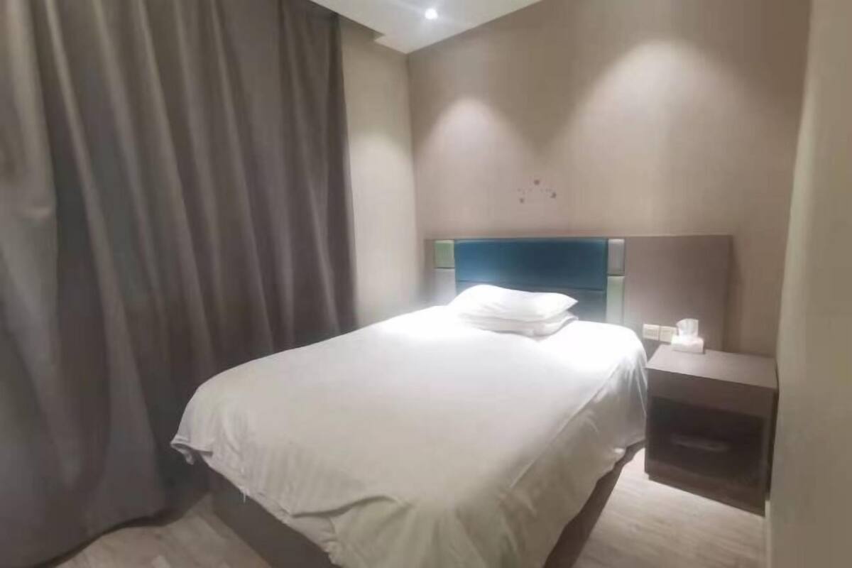 A hotel room with a bed, a nightstand, a lamp, and a curtain.