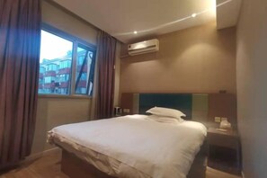 Una habitación de hotel con cama, mesita de noche, ventana con cortinas y aire acondicionado.