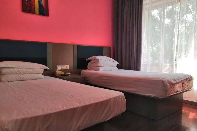 A hotel room with two beds, a nightstand, and a window with curtains.