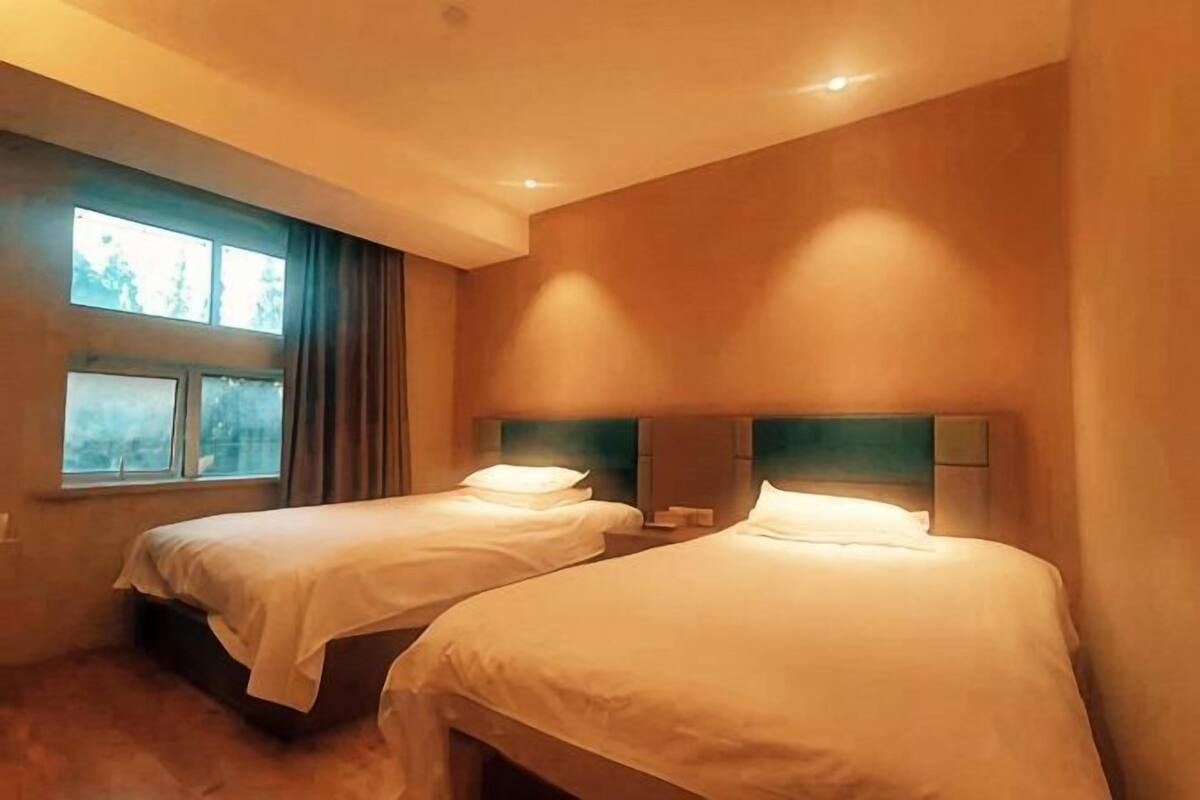 A hotel room with two beds, a window with curtains, and a nightstand.
