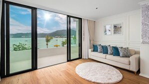 A modern living room with a large sliding glass door leading to a balcony with a view of the sea and hills.