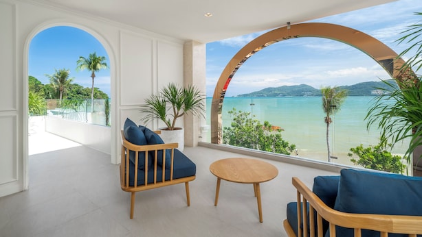 A modern room with a large window offering a view of a beach and palm trees.