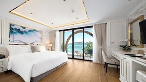 A modern hotel room with a large bed, a desk, and a view of the sea.
