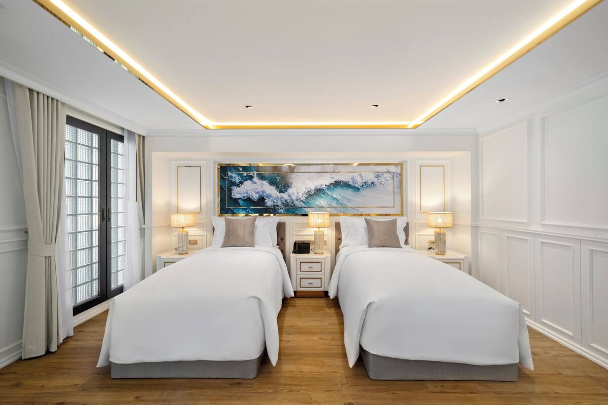 Habitación de hotel con dos camas, una obra de arte grande encima de ellas y una ventana con cortinas.