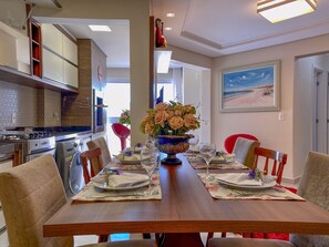 Un comedor con una mesa de madera dispuesta para cuatro personas, rodeada de sillas. Un jarrón grande con flores está colocado en el centro.