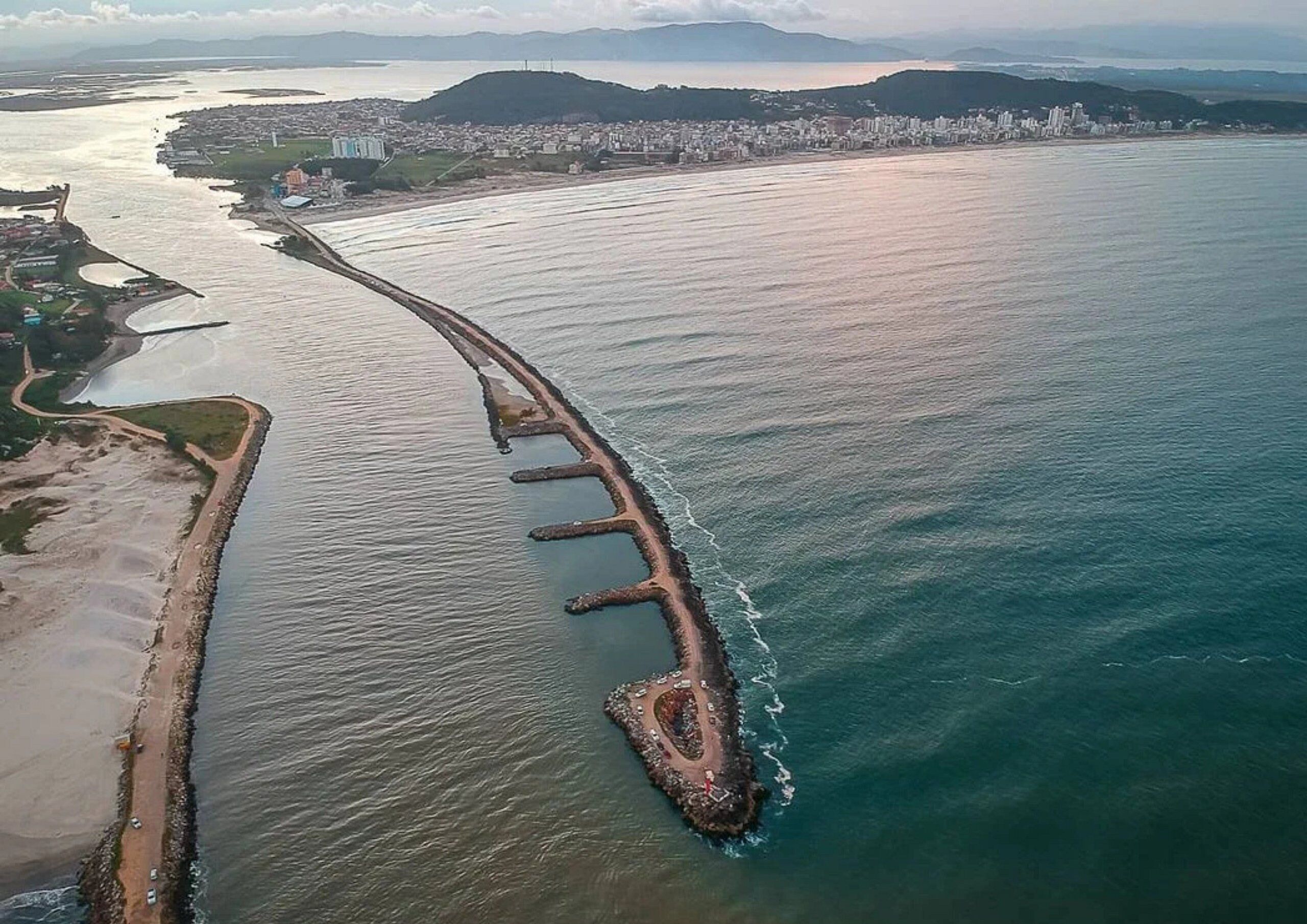 Vista aérea de una ciudad costera con un rompeolas curvo prominente que se adentra en el mar.
