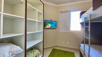 Um quarto com uma cama beliche, um tapete verde, uma televisão na parede e uma janela com persianas.