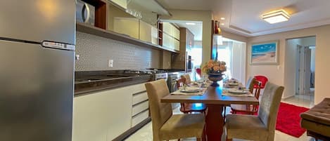 A modern kitchen with a stainless steel refrigerator, a dining area with a wooden table and chairs, and a red rug.