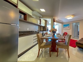Uma cozinha moderna com uma geladeira de aço inoxidável, uma área de jantar com mesa e cadeiras de madeira, e um tapete vermelho.