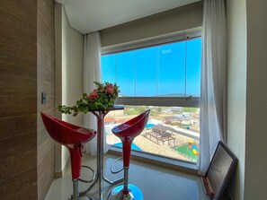 Habitació amb una finestra gran, un tamboret vermell i un ram de flors.