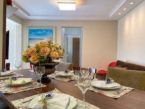 A dining table set with floral placemats, a vase of flowers, and wine glasses. - Resid. Clube Mar Grosso-Laguna - LAG605 (Laguna)