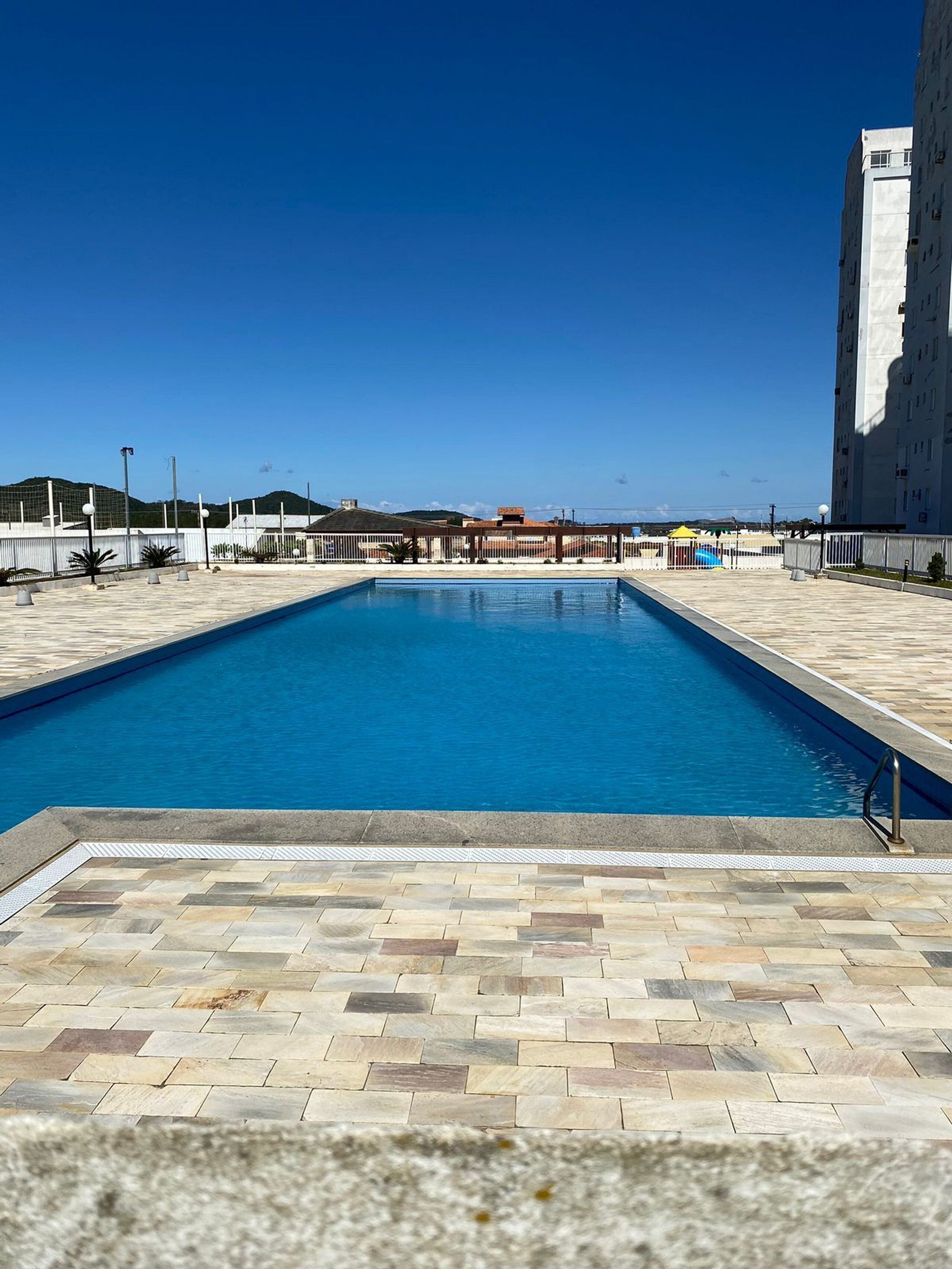 A rectangular swimming pool with a tiled deck, surrounded by a fence and a building.