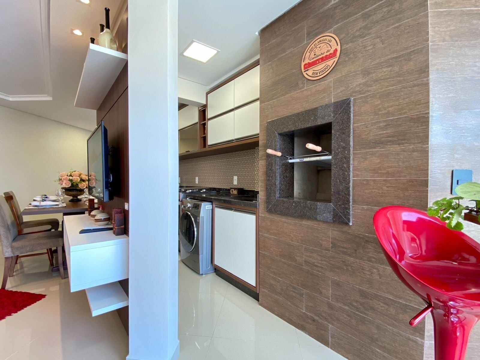 Una cocina moderna con horno integrado, lavadora y comedor con una silla roja y un florero.